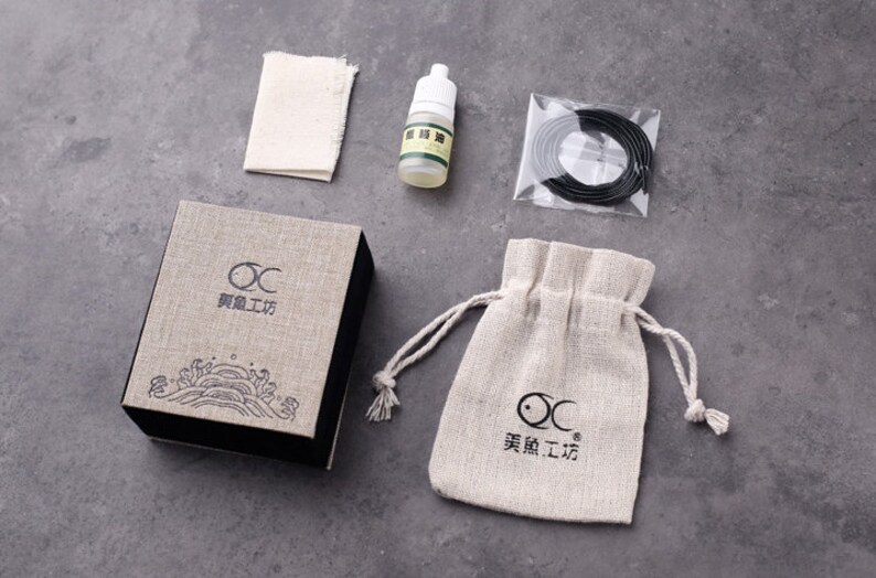 May include: A set of tools for cleaning and maintaining a wooden brush pen. The set includes a small bottle of oil, a cleaning cloth, a small bag, and a roll of black string. The packaging is a brown box with the text "OC 某某工房" printed on it.
