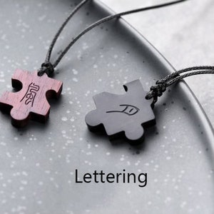 May include: Two wooden puzzle piece pendants on black cords. The pieces are connected by the word "Best" on one piece and a feather design on the other.