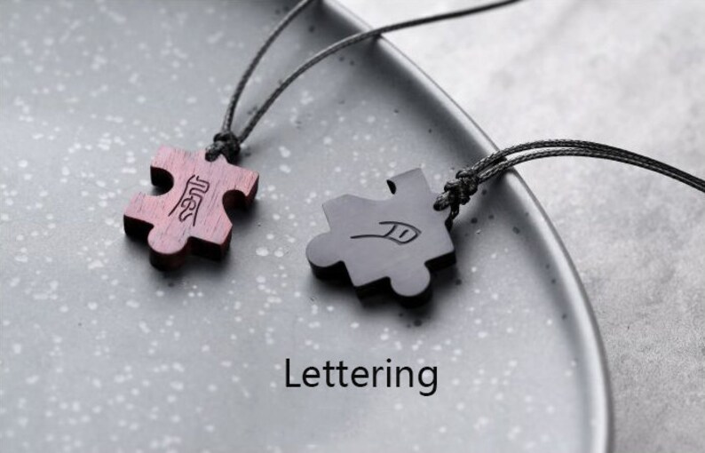 May include: Two wooden puzzle piece pendants on black cords. The pieces are connected by the word "Best" on one piece and a feather design on the other.