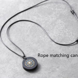 May include: A black leather cord necklace with a round pendant featuring a sun design with gold accents. The cord is adjustable.