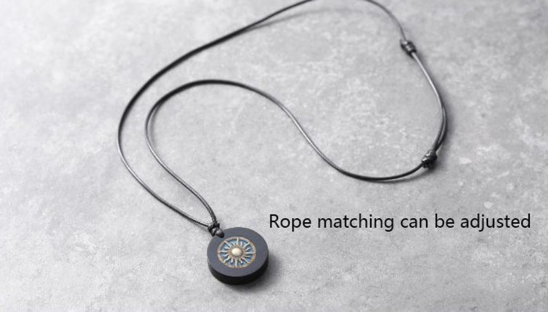 May include: A black leather cord necklace with a round pendant featuring a sun design with gold accents. The cord is adjustable.