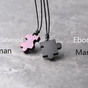 May include: Two wooden puzzle pieces on black cords. The pieces are shaped like puzzle pieces and are made of red sandalwood and ebony wood.