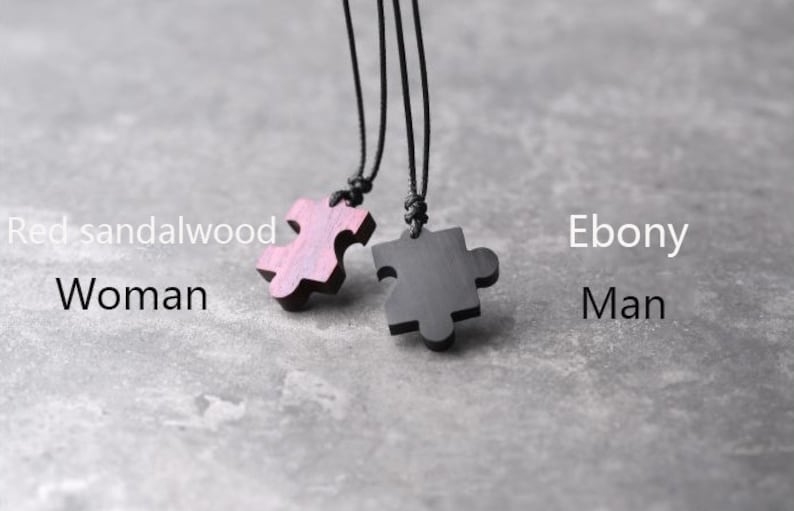 May include: Two wooden puzzle pieces on black cords. The pieces are shaped like puzzle pieces and are made of red sandalwood and ebony wood.