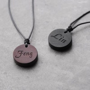 May include: Two wooden necklaces with black cords. The pendants are round and have the names "Feng" and "Lin" engraved on them.