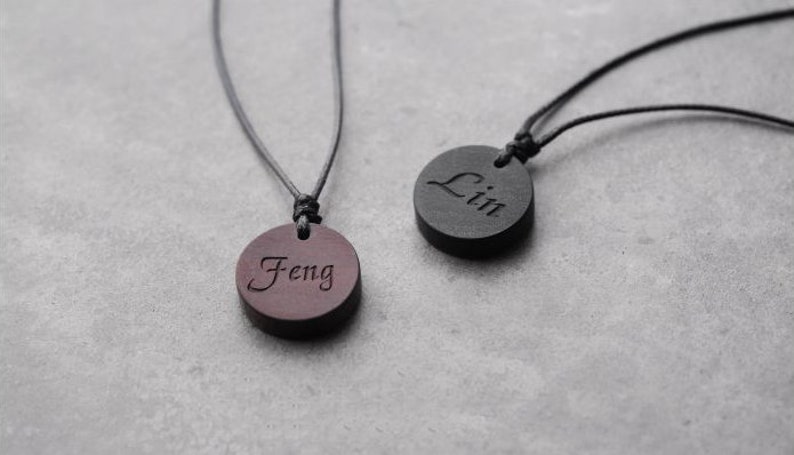 May include: Two wooden necklaces with black cords. The pendants are round and have the names "Feng" and "Lin" engraved on them.