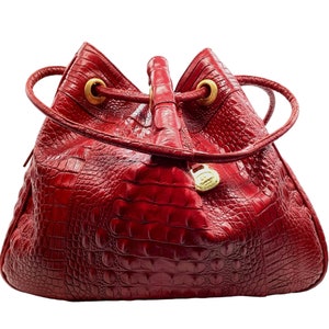 May include: A red crocodile embossed leather handbag with a drawstring closure and gold hardware.