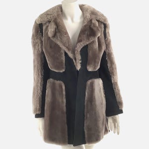 May include: A black and brown faux fur coat with a long sleeve and a collar. The coat has a unique design with panels of faux fur and suede.