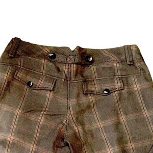 Puede incluir: Primer plano de la parte trasera de unos pantalones a cuadros marrones. Los pantalones tienen dos bolsillos con cierre de bot&oacute;n y botones decorativos en la cintura. El estampado de cuadros es marr&oacute;n y beige.
