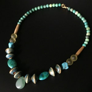 May include: A turquoise and green beaded necklace with a teardrop-shaped pendant. The necklace features a variety of beads, including round, oval, and teardrop shapes.