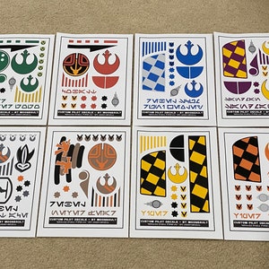 Puede incluir: Ocho hojas de papel blanco con calcomanías personalizadas de piloto en negro y color para un modelo de X-Wing de Star Wars. Las calcomanías presentan el símbolo de la Alianza Rebelde, varios patrones geométricos y texto en Aurebesh, el alfabeto ficticio utilizado en el universo de Star Wars.