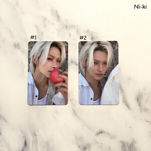 May include: Two rectangular photo cards featuring a person with light blonde hair. One card shows the person holding a red strawberry. The other card shows the person's face. The text "Ni-ki" is in the upper right corner, and the cards are labeled "#1" and "#2".