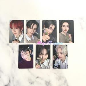 May include: Set of seven photo cards featuring young men holding small white flowers. Each card has a different image of a man with various hair colors and outfits. The background is a marble pattern.