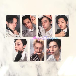 May include: Seven photo cards featuring different young men. Each card displays a head and shoulders shot of a man with various hairstyles and expressions. The cards are arranged on a white and gray marble surface.