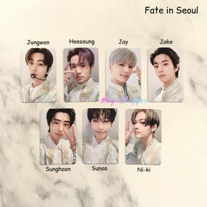 Pode incluir: Um conjunto de 8 cartões de fotos com membros do grupo de K-pop ENHYPEN. Cada cartão apresenta um membro diferente com uma roupa branca e dourada com o texto "Fate in Seoul" no topo da imagem.