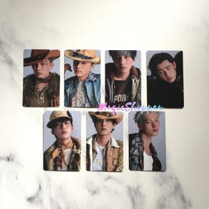 May include: Seven rectangular trading cards featuring images of people in various outfits, including cowboy hats, bandanas, and jackets. The cards have a light gray background and are arranged in two rows.