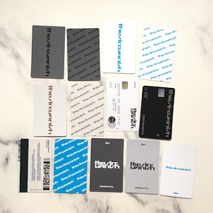 Op de afbeelding: Een verzameling rechthoekige kaarten met de tekst "the/in:Vanish" in verschillende kleuren en stijlen. Sommige kaarten hebben extra tekst en afbeeldingen, waaronder een creditcardontwerp en een streepjescode.