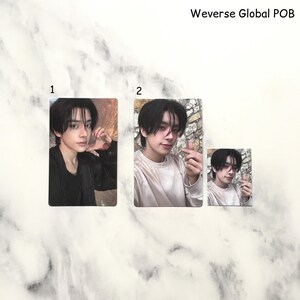 Op de afbeelding: Drie fotokaarten met een persoon met donker haar. De kaarten zijn genummerd 1 en 2, met een kleinere kaart die ook is genummerd 2. De tekst "Weverse Global POB" staat bovenaan. De achtergrond heeft een marmerpatroon.