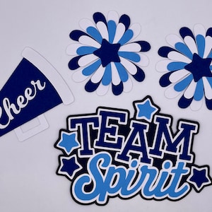 May include: Blue and white paper cutouts for a cheerleading theme. The cutouts include a megaphone with the word "Cheer" on it, two large flowers, and the words "Team Spirit" with stars.