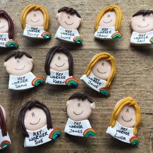 Op de afbeelding: Een verzameling van 12 kleurrijke kleifiguren met regenboogaccenten. Elk figuur heeft een wit label met de tekst "Key Worker" en een naam. De namen zijn: Jamie-Lee, Becky, Luke, Tracy, Ian, Sean, Karen, Jane, Gill, Sue, James en Linda.