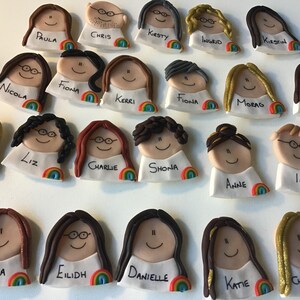 Op de afbeelding: Een verzameling van 20 kleurrijke handgemaakte kleifiguren met regenboogaccenten. Elk figuur heeft een uniek kapsel en gezichtskenmerken. De figuren hebben namen die eronder zijn geschreven, waaronder Paula, Chris, Kirsty, Ingrid, Fiona, Kerri, Nicola, Charlie, Shona, Anne, Liz, Jorven, Lanna, Eilidh, Danielle, Katie en Christine.