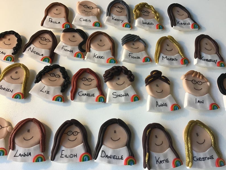 Op de afbeelding: Een verzameling van 20 kleurrijke handgemaakte kleifiguren met regenboogaccenten. Elk figuur heeft een uniek kapsel en gezichtskenmerken. De figuren hebben namen die eronder zijn geschreven, waaronder Paula, Chris, Kirsty, Ingrid, Fiona, Kerri, Nicola, Charlie, Shona, Anne, Liz, Jorven, Lanna, Eilidh, Danielle, Katie en Christine.