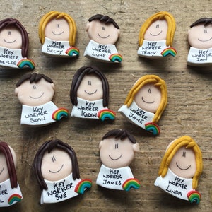 Op de afbeelding: Een verzameling van 10 kleurrijke sleutelwerknemer-badges. Elke badge heeft een cartoon gezicht met een regenboog en de tekst "Sleutelwerknemer" en een naam. De namen zijn Jamie-Lee, Becky, Luke, Tracy, Ian, Sean, Karen, Jane, Gill, Sue, James en Linda.