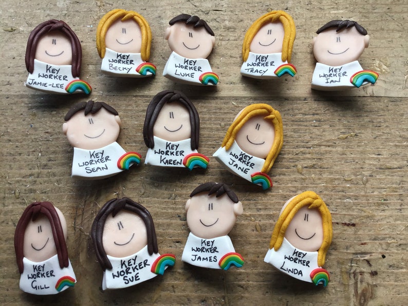 Op de afbeelding: Een verzameling van 12 kleurrijke sleutelwerknemer-badges met regenboogaccenten. Elke badge heeft een cartoongezicht met een naam en de tekst "Sleutelwerknemer" eronder.