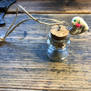 May include: A small glass jar with a cork top and a twine loop. A white heart-shaped ornament with the text "Mr. & Mrs. Barney" is attached to the jar.