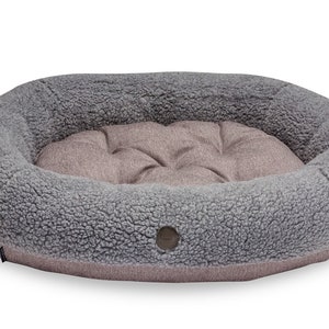 Puede incluir: Una cama para perros ovalada de color gris y marr&oacute;n con una textura suave, mullida y esponjosa. La cama tiene un borde elevado y un centro acolchado.