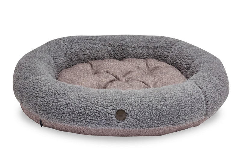 Puede incluir: Una cama para perros ovalada de color gris y marr&oacute;n con una textura suave, mullida y esponjosa. La cama tiene un borde elevado y un centro acolchado.