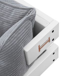 May include: Close-up of a white wooden sofa with a gray corduroy cushion. The sofa has a wooden frame with a white paint finish and a small wooden sign that says "HAMMER & NAIL" on the side.