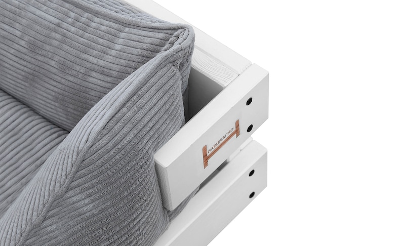 May include: Close-up of a white wooden sofa with a gray corduroy cushion. The sofa has a wooden frame with a white paint finish and a small wooden sign that says "HAMMER & NAIL" on the side.