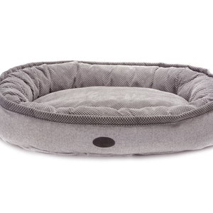May include: A gray oval-shaped dog bed with a raised rim and a soft, plush interior. The bed has a subtle textured pattern and a small gray label on the front.