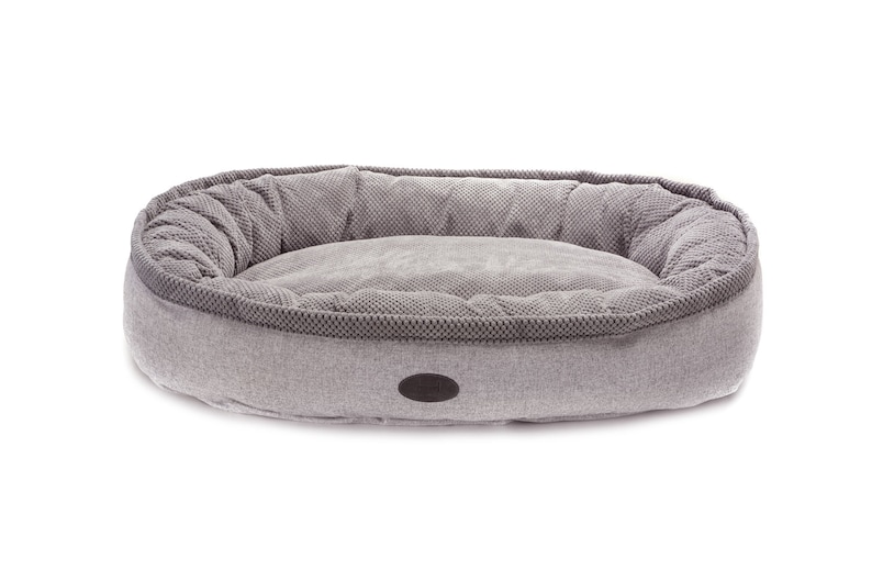 May include: A gray oval-shaped dog bed with a raised rim and a soft, plush interior. The bed has a subtle textured pattern and a small gray label on the front.