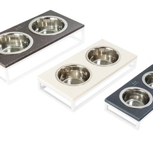 May include: Three elevated pet food and water bowls with stainless steel bowls. The bowls are on a white stand with a brown, white, and gray top.