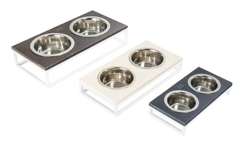 May include: Three elevated pet food and water bowls with stainless steel bowls. The bowls are on a white stand with a brown, white, and gray top.