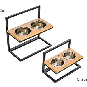 K&ouml;nnte beinhalten: Zwei erh&ouml;hte Hunden&auml;pfe mit einem schwarzen Metallrahmen und einer Holzplattform. Die N&auml;pfe sind aus Edelstahl und die gr&ouml;&szlig;ere Gr&ouml;&szlig;e ist mit "L Size" und die kleinere Gr&ouml;&szlig;e mit "M Size" gekennzeichnet.
