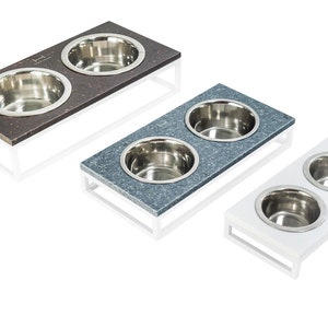 May include: Three elevated pet food and water bowls with stainless steel bowls. The bowls are on a white, gray, and brown platform with a white metal frame.