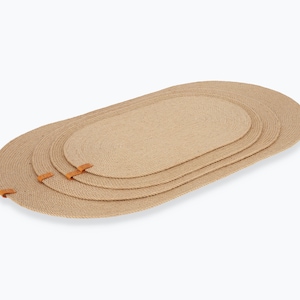 May include: Set of three oval jute placemats with leather trim. The placemats are nested together, with the largest on the bottom and the smallest on top.