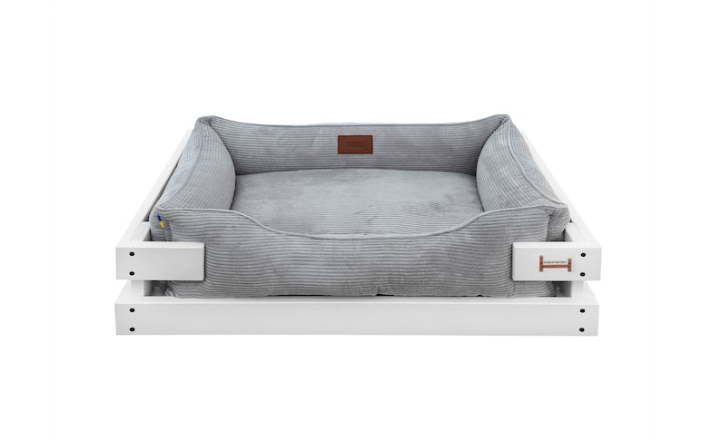 May include: A gray corduroy dog bed with a white wooden frame. The bed has a raised edge and a comfortable, cushioned interior.