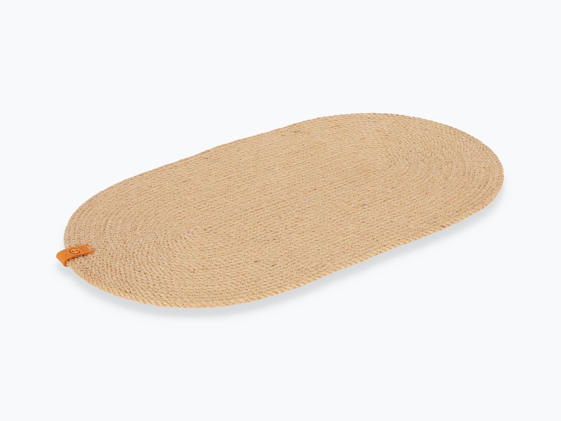 May include: An oval rug made from natural woven rope with a brown leather tag. The rug is beige and has a subtle texture.