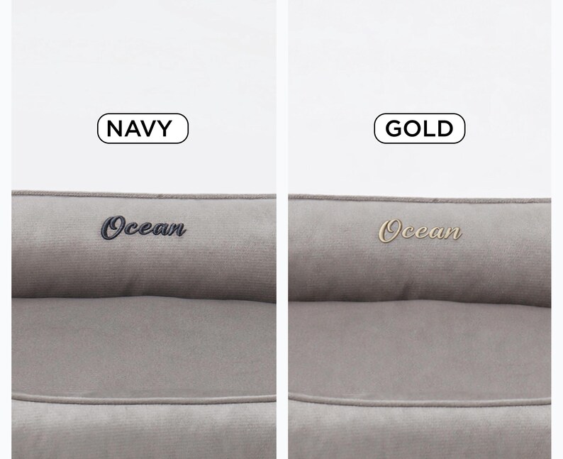 May include: Two pet beds in a neutral gray color. One bed has "Ocean" embroidered in navy blue, and the other has "Ocean" embroidered in gold. The beds have a rectangular shape with a raised bolster.