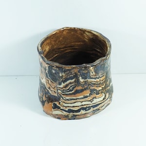 Op de afbeelding: Een bruine, zwarte en witte keramische plantenpot met een golvend, abstract patroon. De pot is gemaakt van aardewerk en heeft een brede, ronde opening.