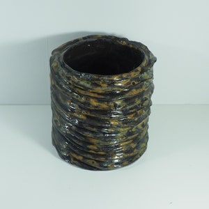 Pode incluir: Um vaso de cerâmica castanho escuro com um design texturizado e ondulado. O vaso tem um acabamento envidraçado e uma forma ligeiramente irregular.