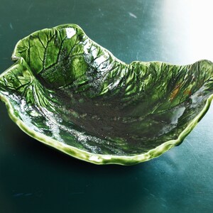May include: A green ceramic bowl shaped like a leaf. The bowl has a textured surface and a glossy finish.