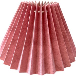 May include: A pink pleated lampshade with a textured surface. The lampshade has a conical shape, with a series of vertical pleats radiating from the center. The color is a muted, dusty rose, and the material appears to be fabric.