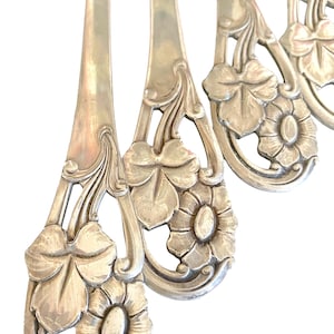 Può includere: Primo piano di posate antiche con disegni floreali e di foglie. Le forchette d'argento hanno manici ornati con intagli dettagliati di fiori e foglie. Le punte delle forchette sono visibili nella parte superiore dell'immagine.