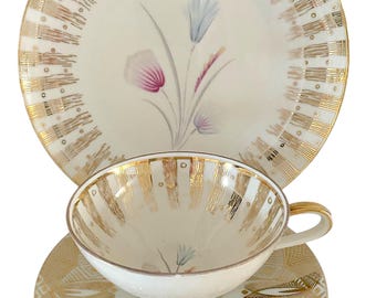 Può includere: Servizio da tè in porcellana vintage con sfondo color crema e dettagli dorati. Il set comprende una tazza, un piattino e un piatto, tutti decorati con un motivo floreale rosa, blu e grigio. I dettagli dorati aggiungono un tocco di eleganza.