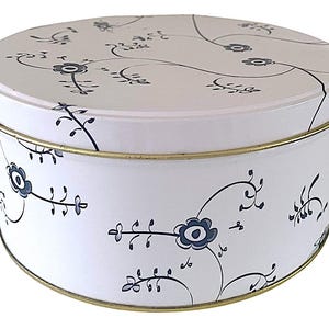 Może przedstawiać: Okrągłe, białe metalowe pudełko z pokrywką, ozdobione niebiesko-czarnym wzorem kwiatowym. Pudełko ma złoty brzeg. Wzór kwiatowy obejmuje stylizowane kwiaty i pnącza, tworząc dekoracyjny wygląd. Idealne do przechowywania.