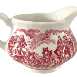 Peut inclure: Crémier en céramique de couleur crème avec un motif rouge. Le motif représente une scène rurale avec une calèche et une maison. Le crémier a une anse et un bec verseur.